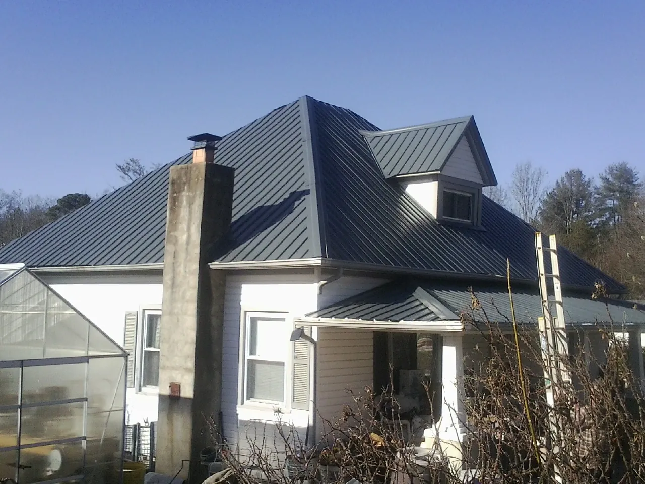 Dark blue standing seam metal roof on a white farmhouse with dormer — Slate & Tile Roof Repair by Roofing Brothers in Pruden