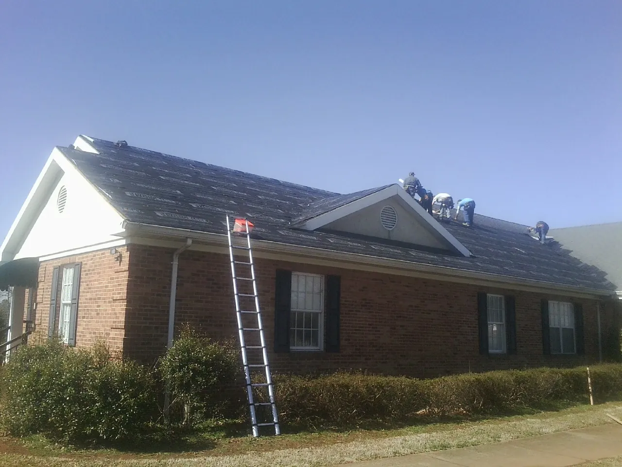 Crew tearing shingles off a brick ranch roof with a ladder set — Metal Roof Repair work by our crew in Pruden