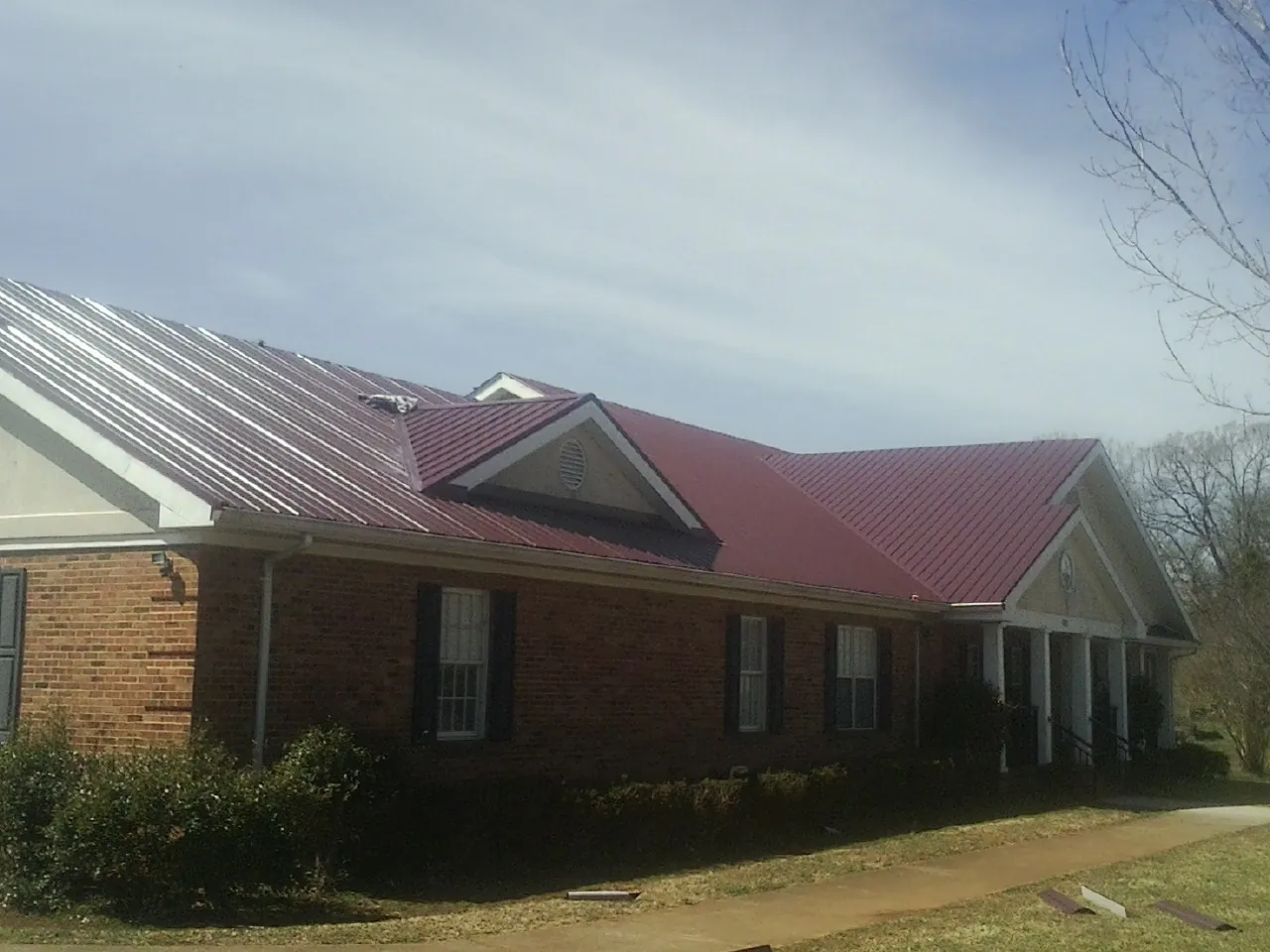 Red metal roof with gabled entries on a long brick building, from a Hail Damage Roof Repair job in Pruden