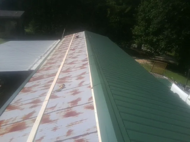 Old rusted panels beside newly installed green metal roofing — Wind Damage Roof Repair by Roofing Brothers in Pruden