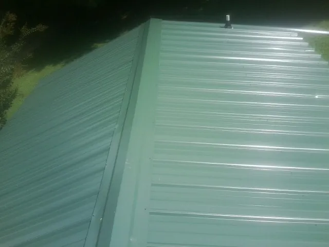 New green metal panels meeting at the ridge of a roof — Flat Roof Repair work by our crew in Pruden