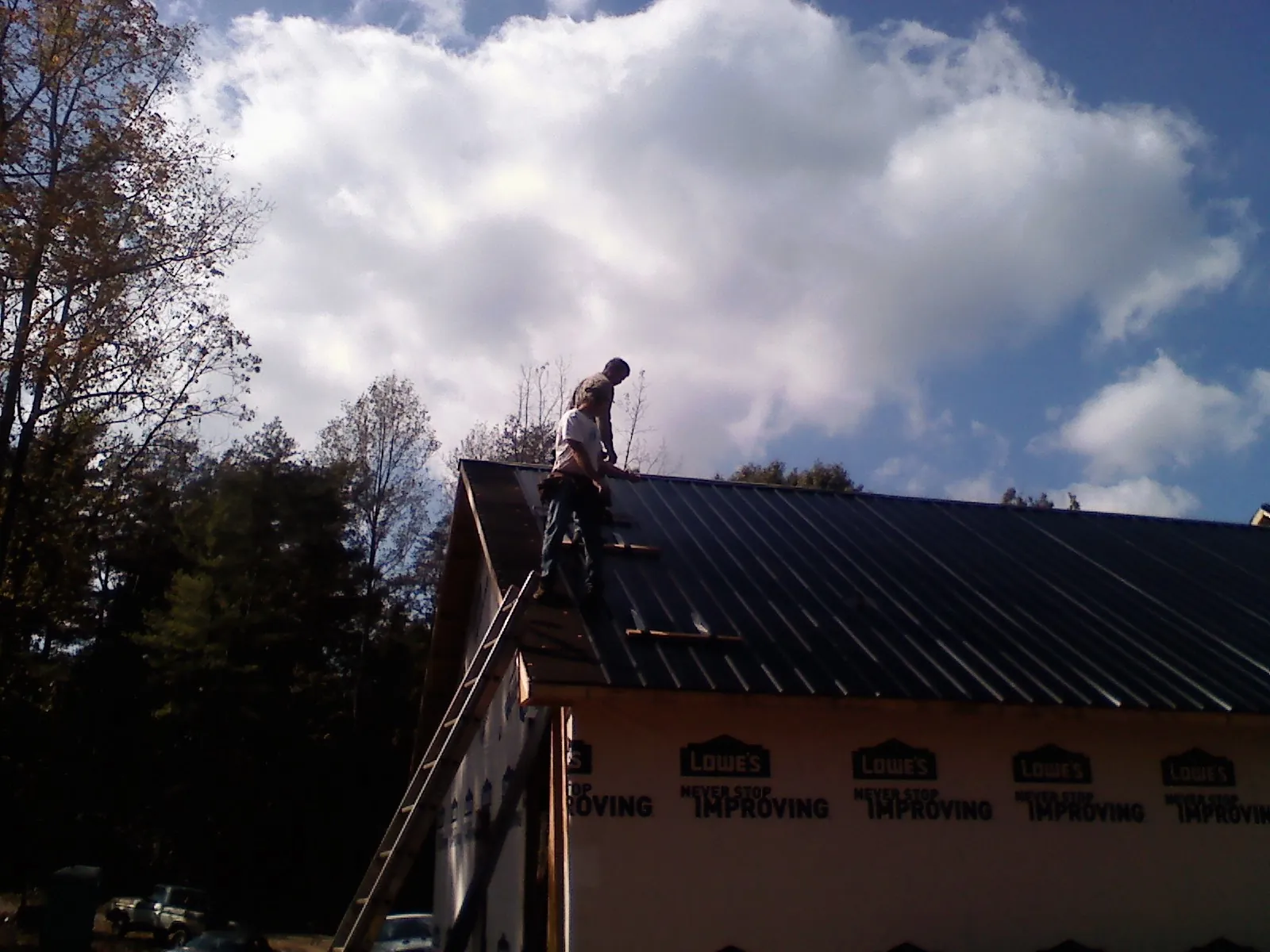 Roofer fastening dark metal panels high against a cloudy sky, from a Roof Inspection job in Pruden