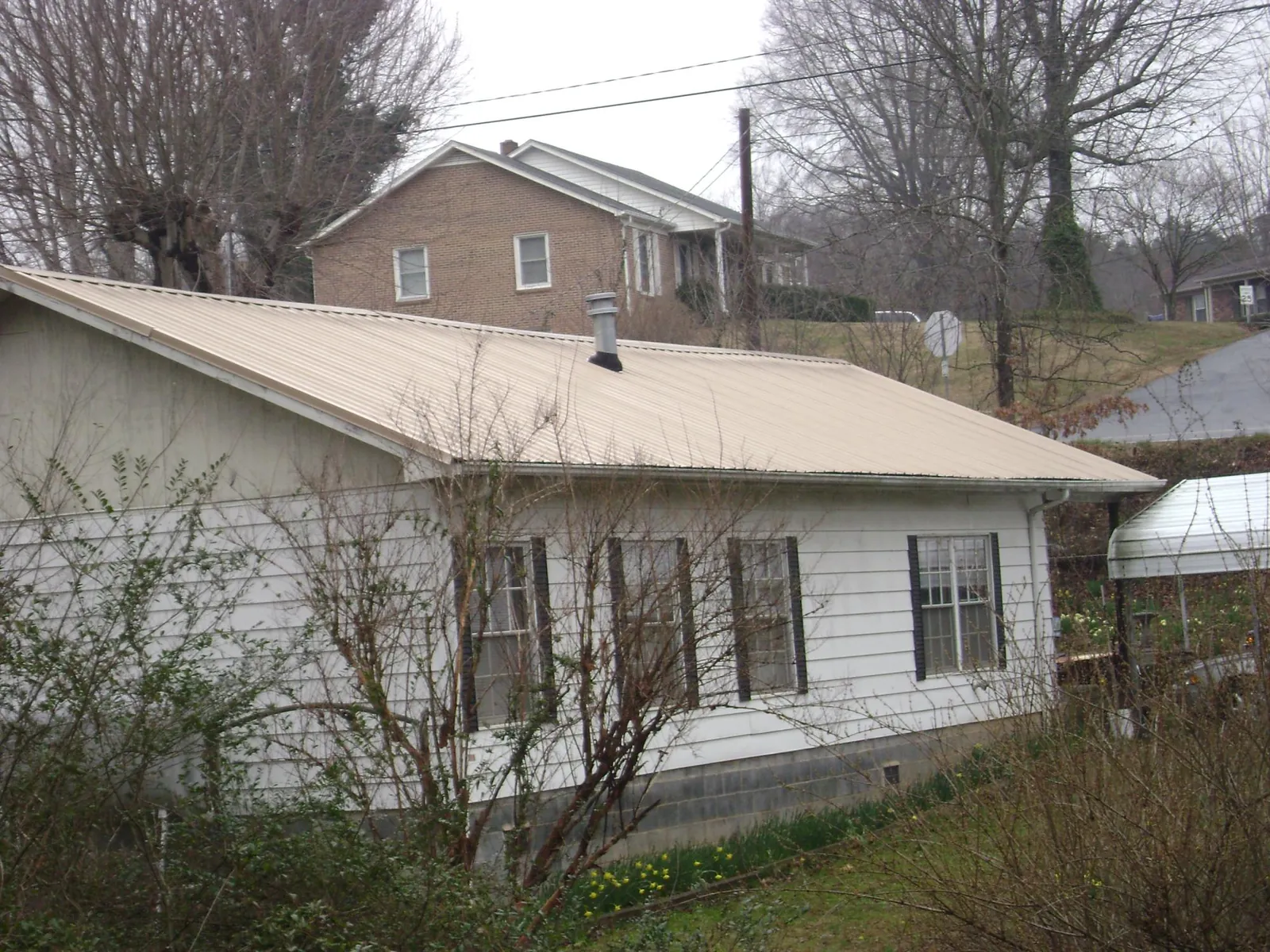 Tan metal roof on a white sided house set into a hillside — Commercial Roofing by Roofing Brothers in Pruden