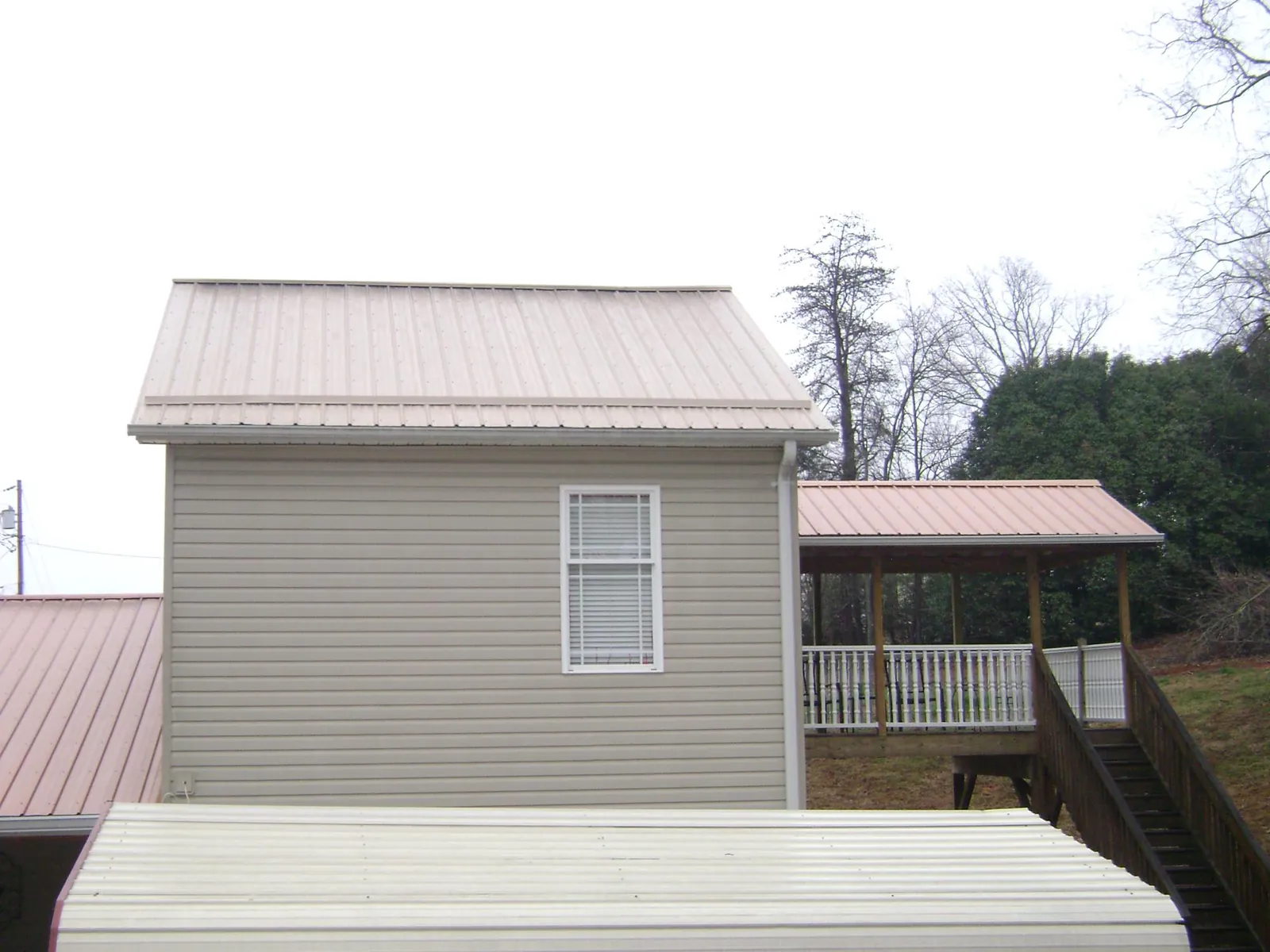 Tan metal roofs on a two story addition and attached porch, from a Roof Replacement job in Pruden